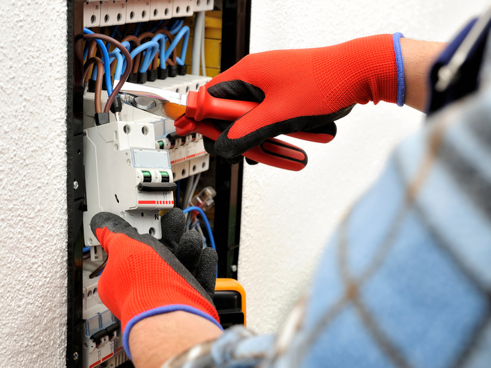 Young electrician technician at work on a electrical panel with protective gloves